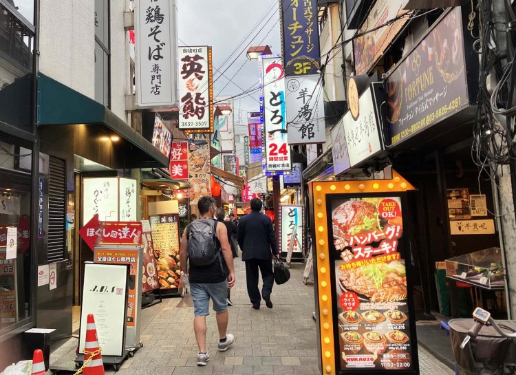 両側から看板が迫り出すにぎやかな飲食店街。色があふれる通りにあってモノトーンの看板が目を引く。