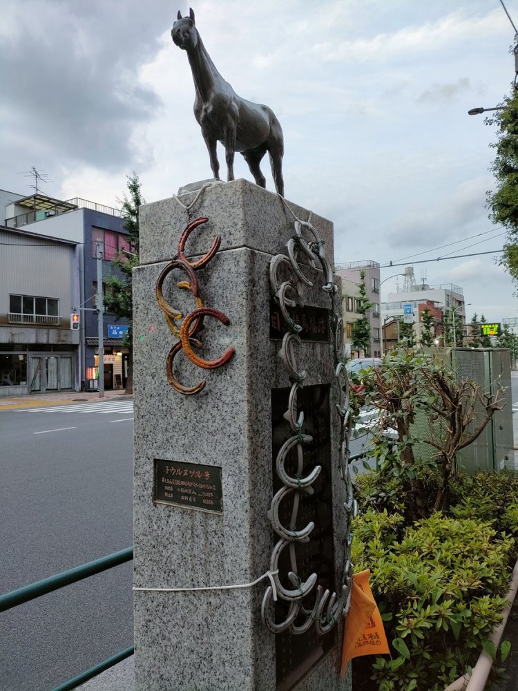 元競馬場交差点付近にある目黒競馬場の碑。蹄がいくつもぶら下がっている。銅像の馬は「トウルヌソル」。英国で大活躍したあと種牝馬として日本へ輸入されて優勝馬を輩出した。