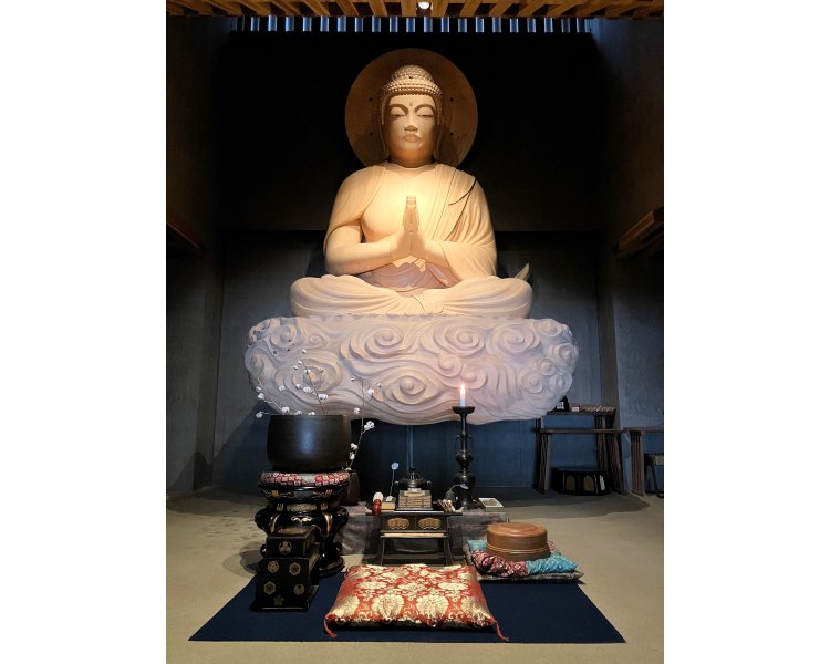 仏師・渡邊勢山氏の手による檜造りの釈迦如来座像。雲と蓮華の座に乗った姿を描く。二丈と呼ばれる約4.6mの高さに圧倒される。仏前に供えられた綿の枝は、厚木の別院で育てられたもの。