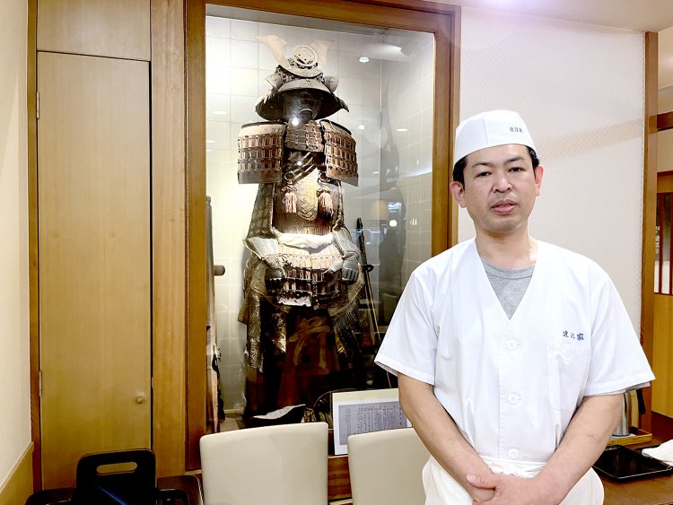 4代目の永谷泰一さん。後ろには先代が集めた鉄砲組百人隊の装束と鉄砲が展示されている。