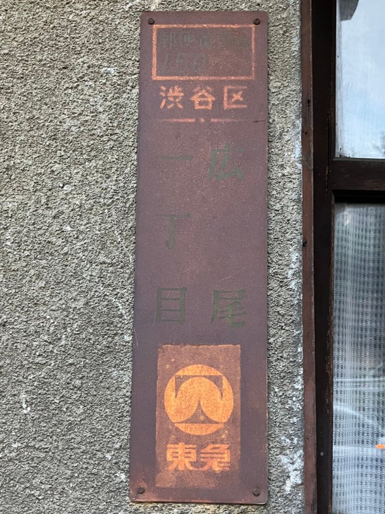 広尾には古い建物も多く残されており、こうした町名表示板も発見することができる。よく見れば、郵便局のキャラクターや東急の広告が見える。