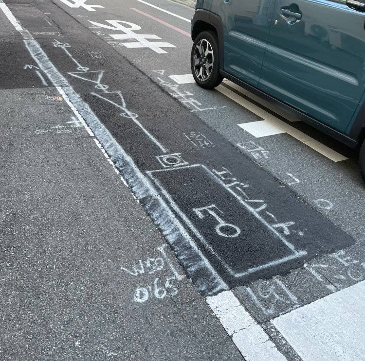 工事中のつぎはぎのアスファルト。地面に埋まっているものがメモされている。工事中しか見られない風景。