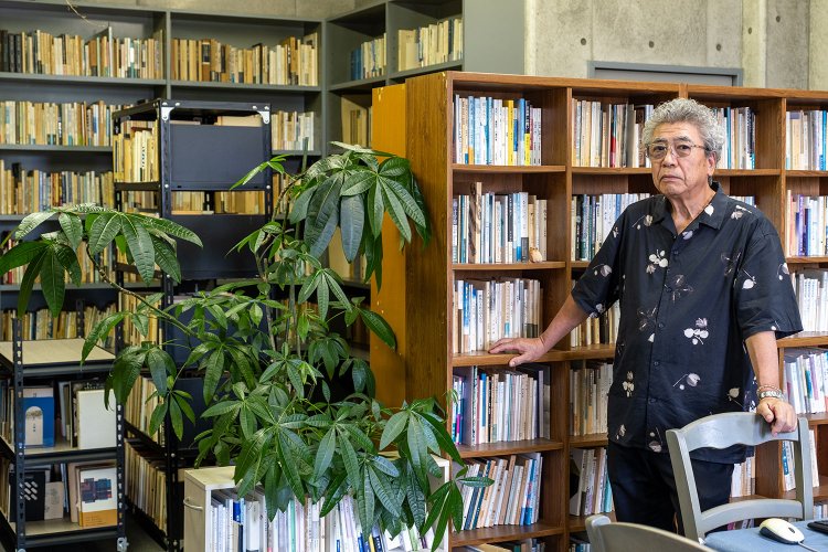 蔵書を前にした富沢さん。個人誌『水の呪文』の発行は2023年春現在55号を数える。