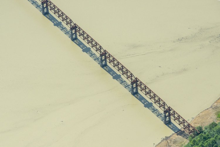 褐色に濁るシューパロ湖の湖面に三弦橋のフォルムが浮かび上がる。東方向から撮影した。