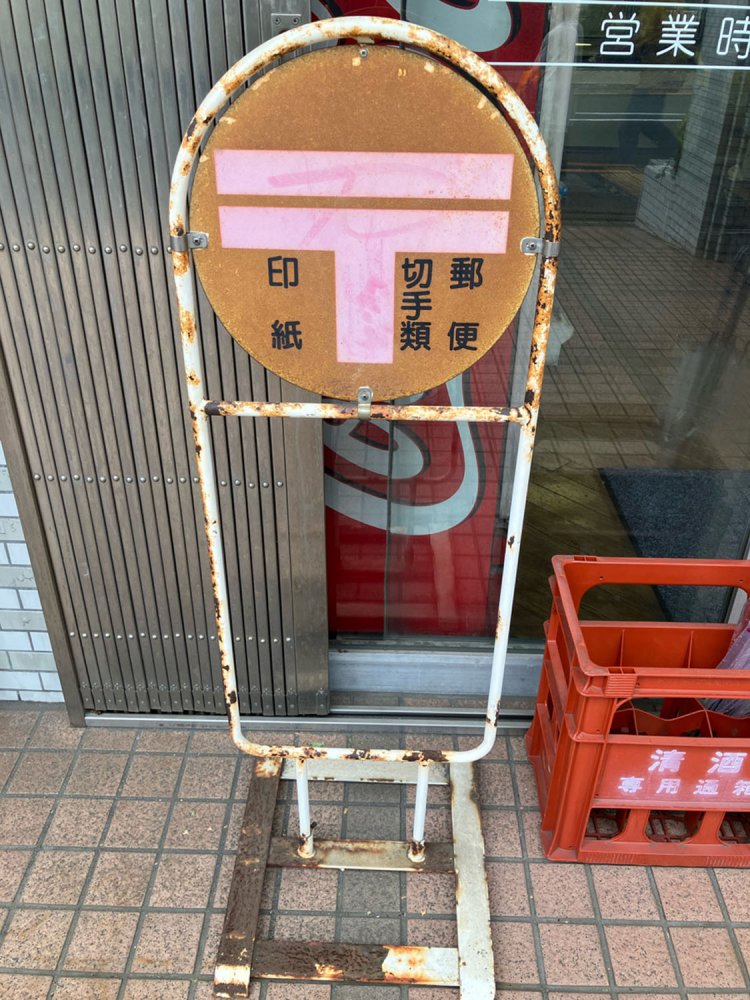 現役で稼働する置き看板。〒マークにうっすら赤みが残る（上用賀）。