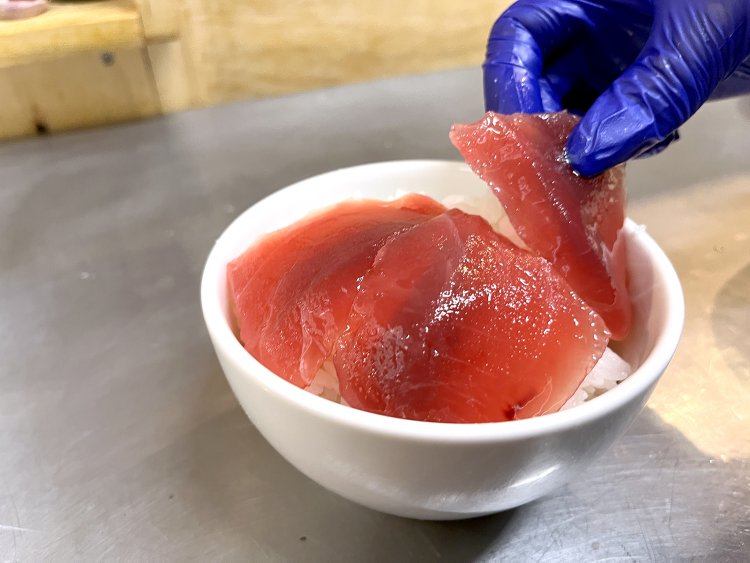 マグロの切り身に醤油ベースのつけだれをくぐらせ、盛り付ける。