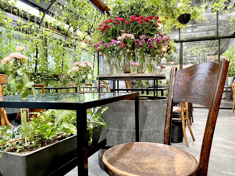 緑のカーテンが周囲を覆い、テーブルの上には季節の花、テーブルの下にはプランターに植え込まれた緑が見える。