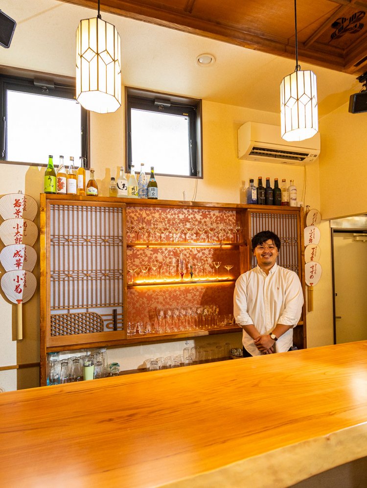 カウンターに立つ店主の峯岸峻吾さん。グラス棚は建具を活用。「各部屋の違いを楽しんで、好きな席でお過ごしください」
