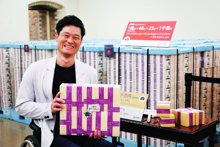 「ウエイトトレーニングの10kgより重く感じる！」／ 1億円を持つ。後ろにあるのは1千億円分の模擬券。