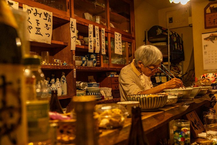 店主の安藤さん。見事な一枚板のカウンターには、手づくりの滋味あふれる総菜が並ぶ。