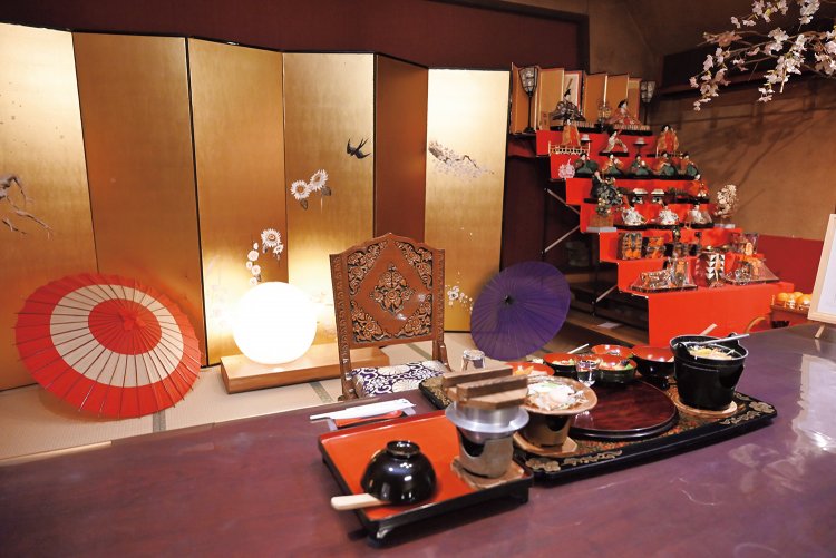 ももこさんが季節の植物を描いた金屛風の前で、夕食をいただく。タイ・チェンマイで造られたテーブルはチーク材。