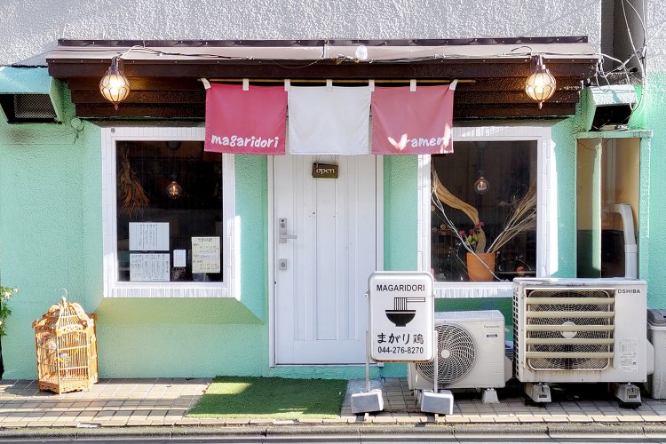 ライトグリーンの外壁に、白い扉、紅白ののれんが映える。