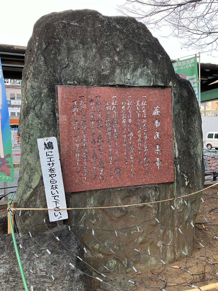 蕨駅前の石碑型市民憲章。周囲には蕨を舞台としたアニメののぼりが一面に立てられ、全く目立たない。