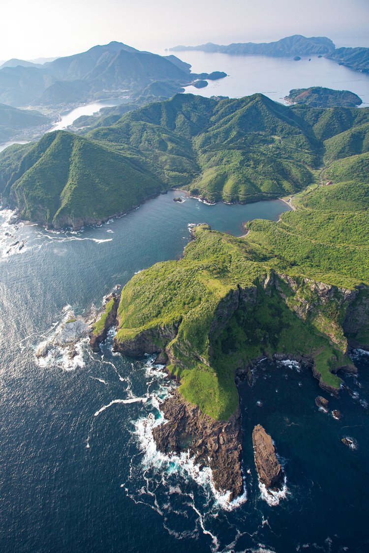 海から垂直に切り立つ崖。手前に亀島、奥に西ノ町の集落や焼火山（たくひやま）も見える