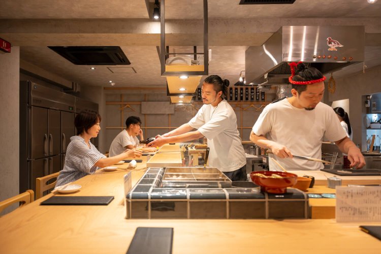 コの字カウンターでBGMはラジオ。タイラガイの海苔巻きを手渡しするお通しもユニーク。「サプライズのおもてなしもお楽しみに！」。