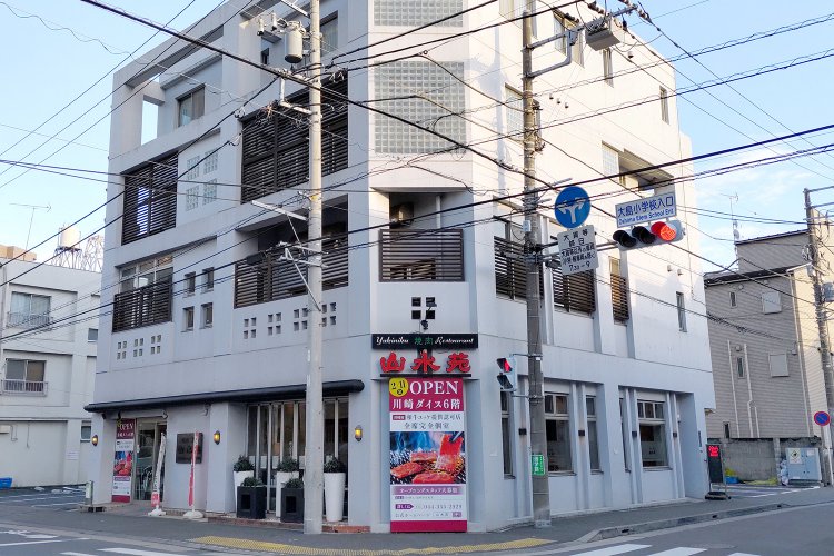 十字路に面したビルの1～2階が店舗として使われている。建物の隣に駐車場あり。