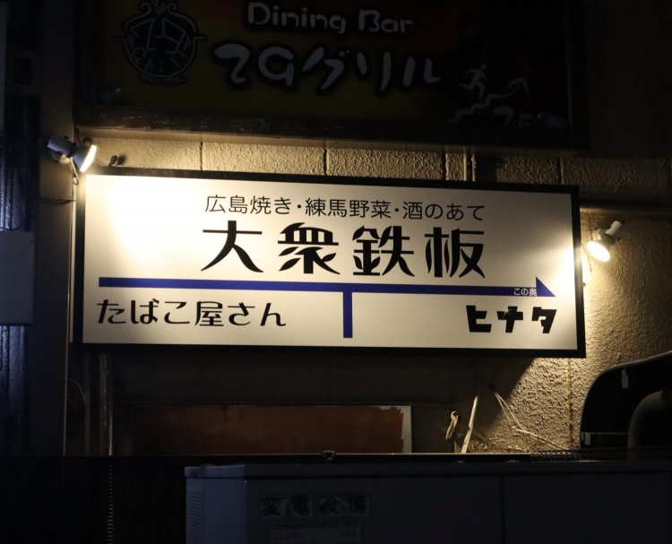タバコ屋ビルの壁にかけられている看板。目を引くなあ～。タバコ屋のビルに、『大衆鉄板ヒナタ』などが入っている。
