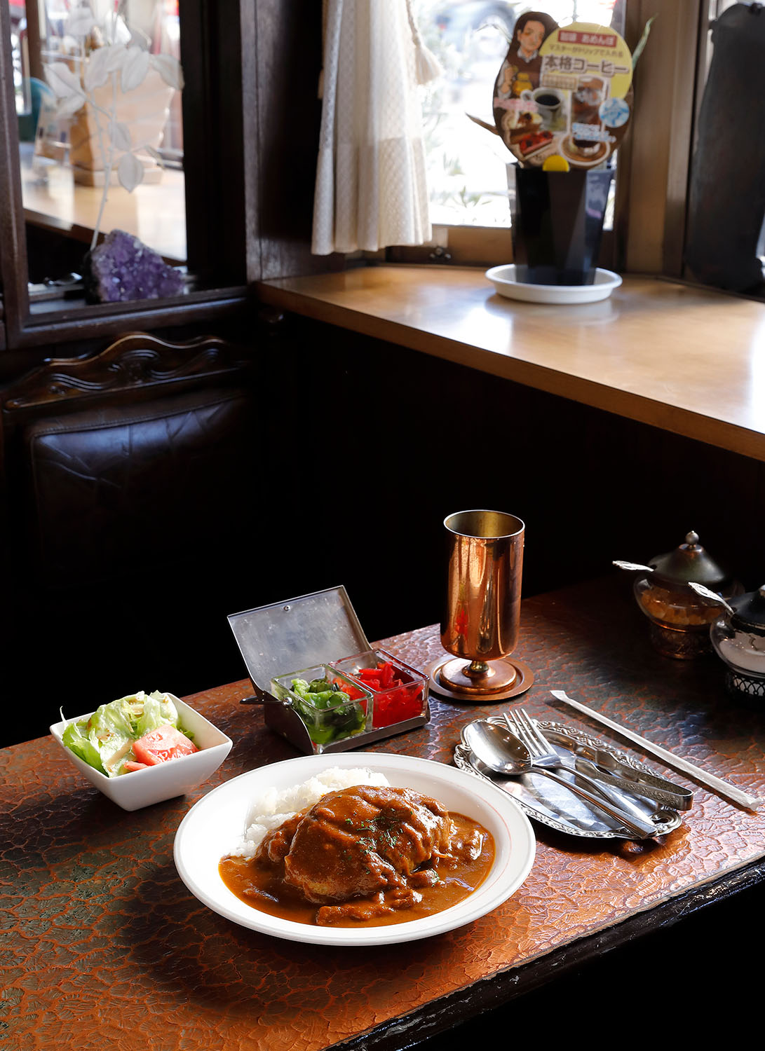 肉厚のハンバーグが鎮座するハンバーグカレー1300円は、サラダ、ドリンク付きセット1580円。アイスコーヒーは銅製グラスで供される。