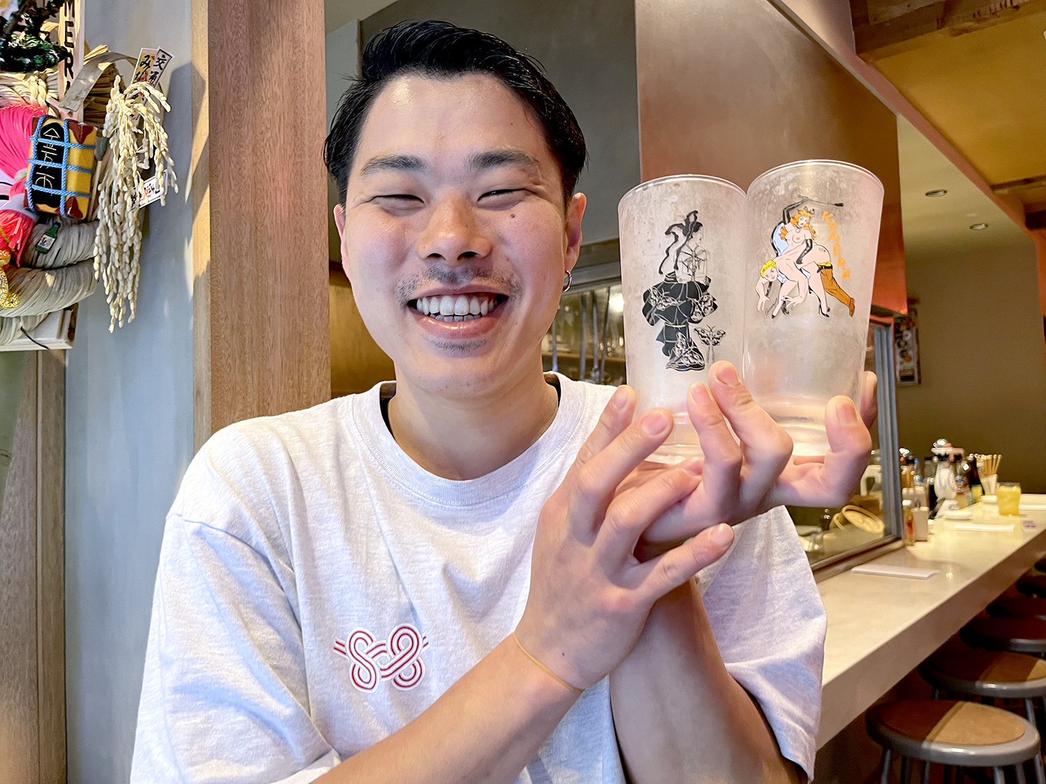 「店内に飾ってあるイラストレーター・寿司テルヤさんの春画のオリジナルグラスもあります」と語るスタッフのせいやさん。