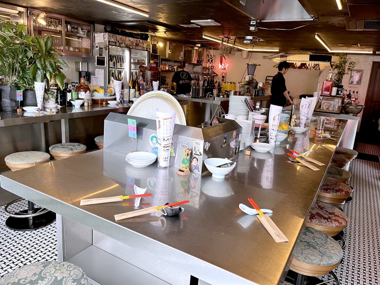 調理台のようなステンレスのテーブルが並んでいる。奥には“餃子”のネオンサインが見える。