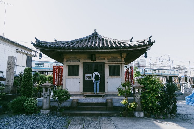 JRと京急の線路にちょうど挟まれた場所にある慶運寺の境内。奥にJRの電車が通過中。