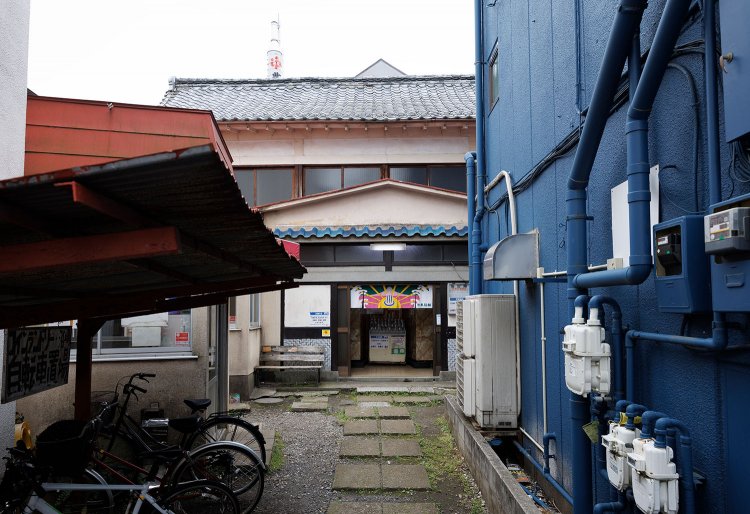 商店街から少しはずれた路地裏にある。後方には煙突。