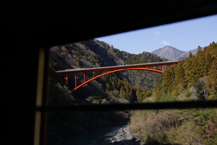 道路が並走しない区間も多く、井川線に乗らないと見られない風景が連続。列車の速度はゆっくりで、ビュースポットでは随時、観光案内や徐行運転をしてくれる。赤い橋は泉大橋で、その奥には朝日岳が見える。