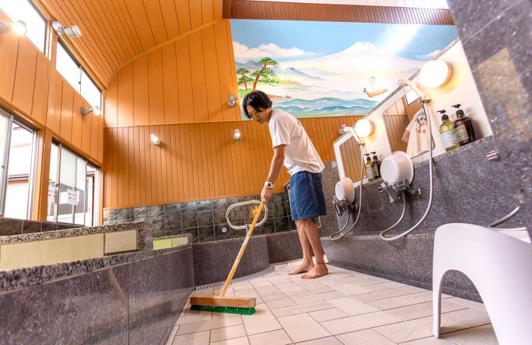 男湯の浴室を清掃する3代目の山本寛太郎さん。弟の彬善（あきよし）さんと切り盛りする。「照明を多くして明るい雰囲気になりました」。