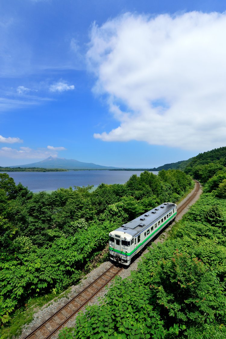 沼の向こうに見えるのは北海道駒ヶ岳。函館本線 仁山（にやま）～大沼間（写真＝マシマ・レイルウェイ・ピクチャーズ）。