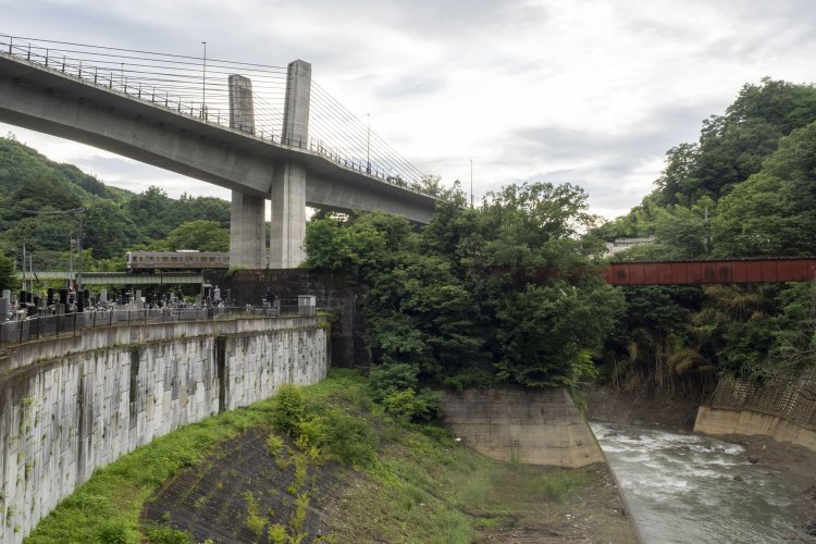白砂川橋梁（写真右の赤い橋桁）と万座・鹿沢口行き211系電車。双方の距離は近い。