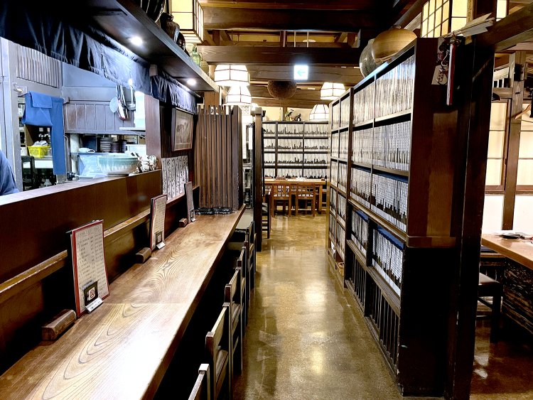 ヒノキの1枚板のカウンターの奥にテーブル席が広がる。ノートが収められた本棚がいい具合に仕切りとなっている。