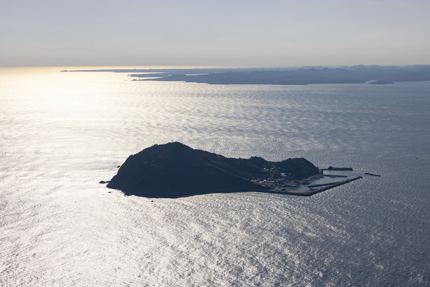 逆光でシルエットとなった神島。奥には志摩半島が見える。