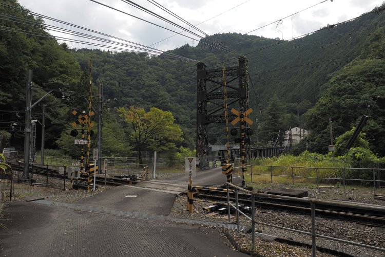 市代踏切から見える市代吊橋。鉄道橋だったときはこの踏切も存在せず、写真手前付近で線路が右へカーブしていたとのこと。アプトいちしろ駅。2024年8月16日撮影。