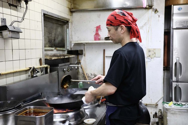 厨房で手際よく鍋を振る福永さん。