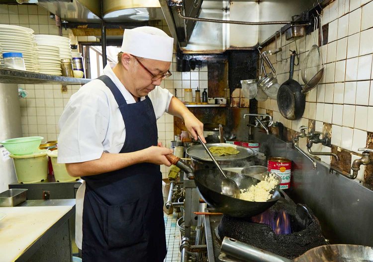 厨房で鍋を振る3代目の岡田亮祐さん。