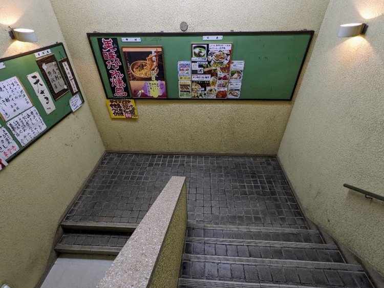 踊り場には掲示板。さらに地下へと続く階段。