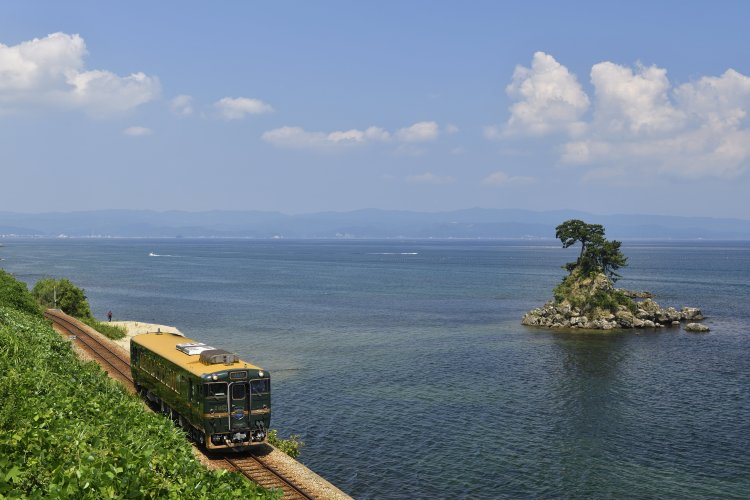 雨晴海岸の先に浮かぶ女岩で一時停止。富山 湾の向こうは能登半島。雨晴〜越中国分間（写真＝レイルマンフォトオフィス）。