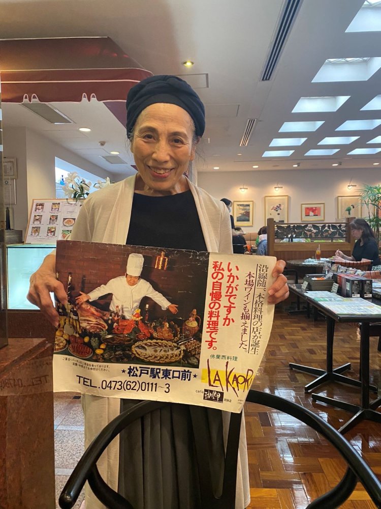 レストランオープン当時の記念すべきポスターを携えるマダム。
