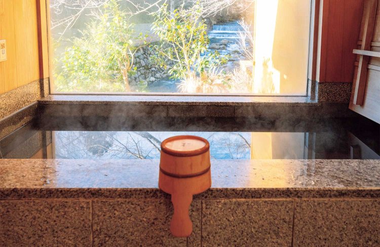 窓の外に八王子川を望む浴室。湯船は黒御影石。以前は温泉だったが、現在は井戸水を張る。