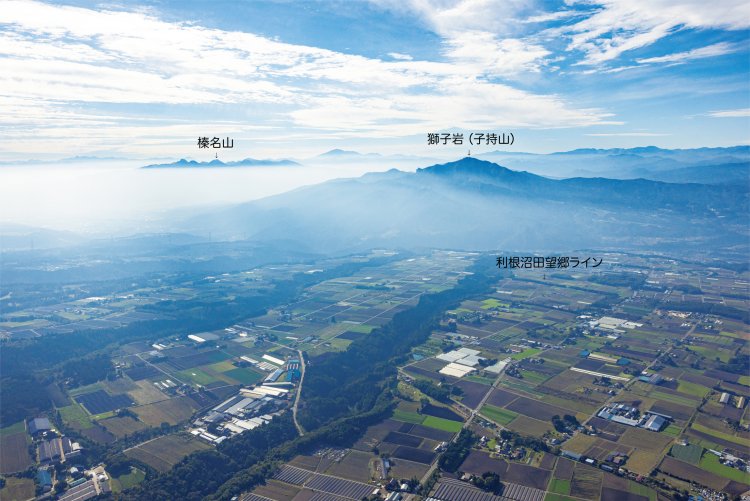 昭和村の上空から南西方面を望む。写真左が前橋・高崎方向、右が水上・越後湯沢方向。獅子岩（子持山）の手前では利根川が流れ、関越自動車道、JR上越線が走る。伊香保温泉は、左奥の榛名山の手前にある。