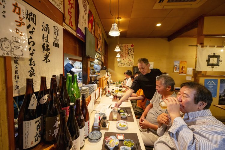 お客さんと談笑する『〼～かまどのある家・酒をよぶ食卓～』の店主･阿部洋祐さん。