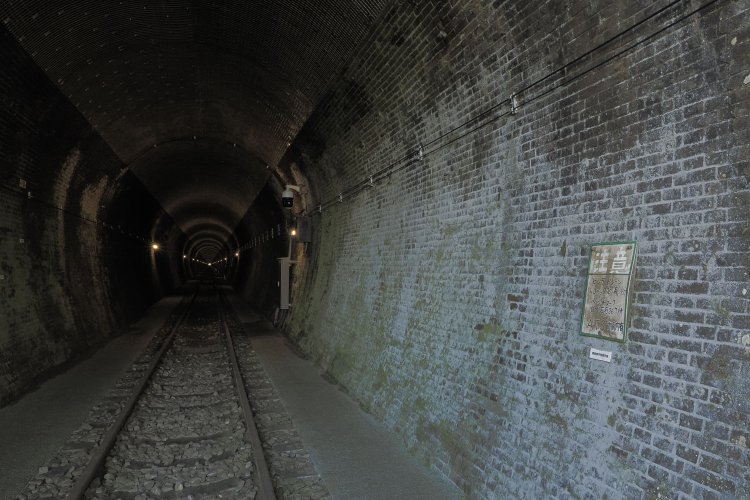 いよいよトンネルへ。中心部はレールが敷かれたまま。バラストと枕木もあって足場は良くない。壁面には保線作業員用の注意書きが残る。