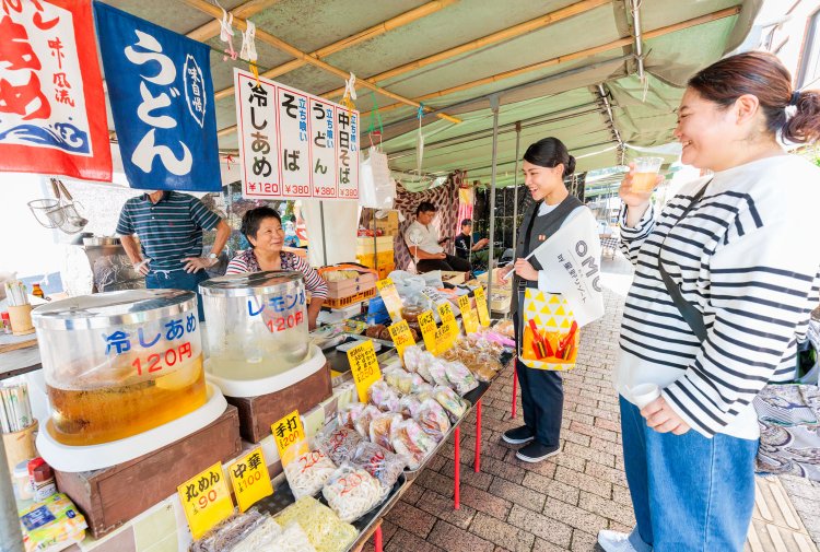 木曜市に到着。池内さんの姿を見て一段と笑顔になる出店者。冷しあめやいも天の試食も楽しめる。