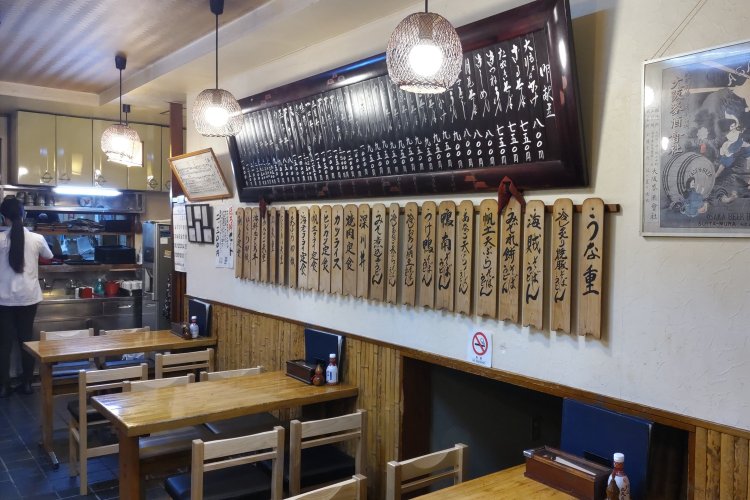4人掛けのテーブル席が並ぶ1階。壁のメニュー名が書かれた木札から歴史が感じられる。