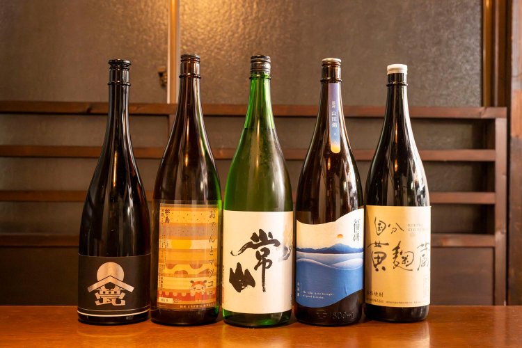 日本酒は定番の「常山」「松の寿」を含め約20種。プレミア酒を除き半合550円、1合990円。焼酎は、「黄麹蔵」（右端）など国分酒造のものを幅広く揃える。