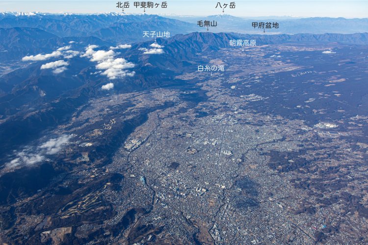 手前に富士宮市中心街、その上に朝霧高原と天子山地、奥に甲府盆地と八ヶ岳が見え、その先にはうっすらと北アルプスも。