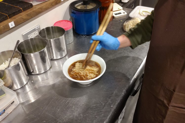器に注いだスープの中へ茹で上がった麺を投入してから、麺の線をキレイに整える。
