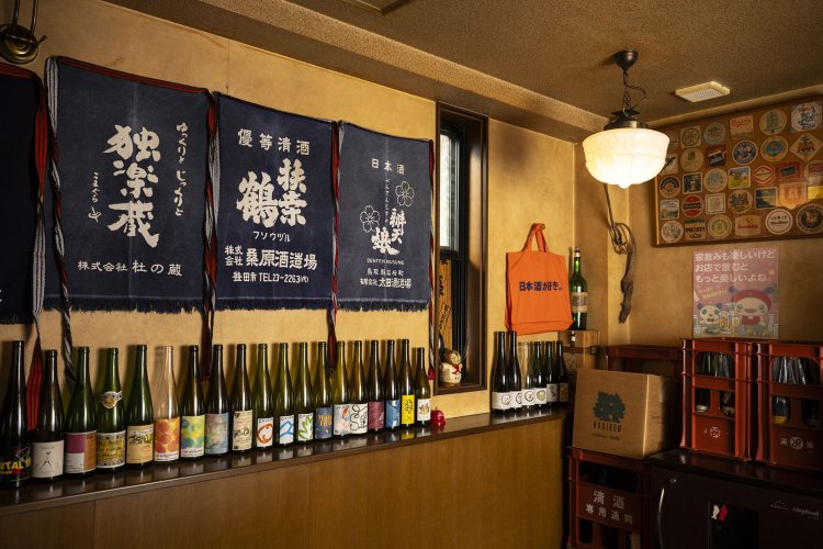 愛すべき燗酒向きの日本酒やワインのボトルが並ぶ。カウンター席中心で営業中。