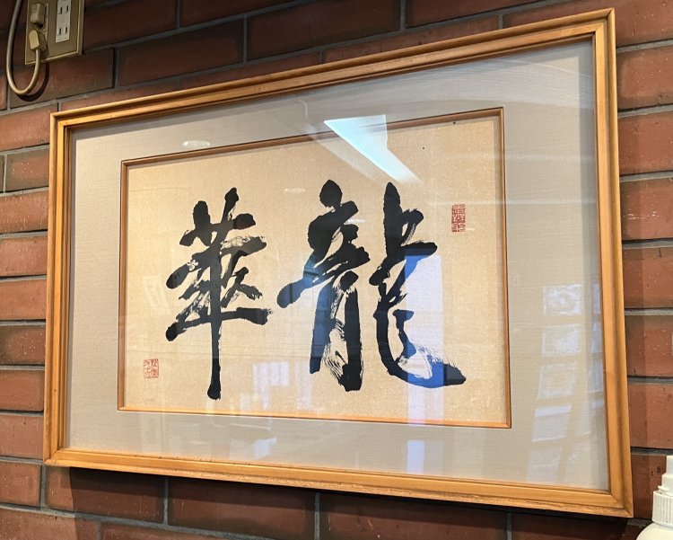 「山水楼」の会長が書いてくれた店名の書。『華』の字の中には4つの人が入っていて「店にたくさんの人が来るように」という願いが込められている。