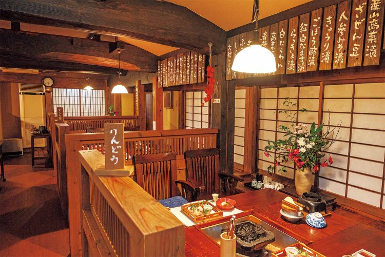 囲炉裏のテーブルを備えた食事処。手書きの漬物のお品書きが掲げられ、温かみを感じる。